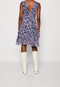 Robe à imprimé floral avec un dos en V profond, un corsage ajusté et une jupe évasée. Associée à des bottes blanches montantes. Palette de couleurs comprenant violet, rose et bleu.