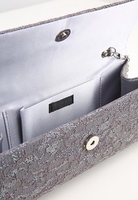 Grå quiltad clutch med intrikata pärl- och spetsmönster, med magnetisk knappstängning, inre ficka och en slät satinfoder.