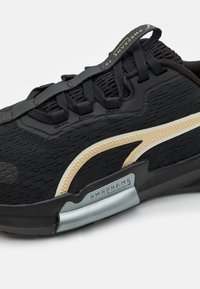 Černá sportovní bota s texturovaným svrškem, zlatými akcenty a šedou mezipodešví, na které je branding "PWRFRAME" a polstrovaný systém šněrování.