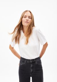Witte v-hals T-shirt met korte mouwen, gecombineerd met hoge taille zwarte jeans. Eenvoudig ontwerp, gladde textuur, geen zichtbare patronen.