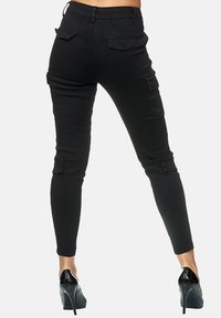 Black cargo pants with a fitted design, featuring large side and back pockets, tapered legs, and a stretchy texture, paired with high heels.