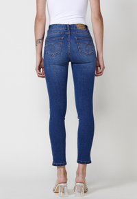 Skinny blue denim jeans with a high waist, featuring two back pockets and a branded tan leather patch at the waistband.