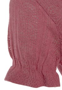 Knit-top vaaleanpunaisena, jossa on teksturoitu kuvio avosilmukoilla. Vyötäröltä istuva ja hihannoissa kerrostettu yksityiskohta.