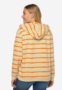 Světlý béžový hoodie s výraznými oranžovými vodorovnými pruhy, kapucí na šňůrku a žebrovanými manžetami na rukávech a spodním lemu.