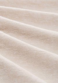 Tela color beige claro con un aspecto texturizado y tejido, que presenta suaves pliegues y sutiles variaciones en tono y textura.