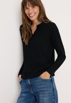 Haut noir à manches longues avec col en V, fabriqué en tissu lisse. Porté avec un jean bleu clair avec poches latérales.