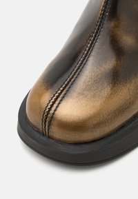 Bout de chaussure en cuir marron avec couture centrale et semelle en caoutchouc noir sur fond blanc.
