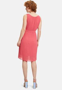 Sleeveless koral kjole med plisseret ryg, strammet talje og udskilt skørt. Båret med sølvfarvede blokhælede sandaler.