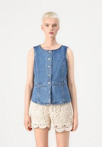 Denim vest med rund hals, frontknapper og to lommer, parret med kremfargede blonder-shorts med bølgede kanter og blomsterdesign.