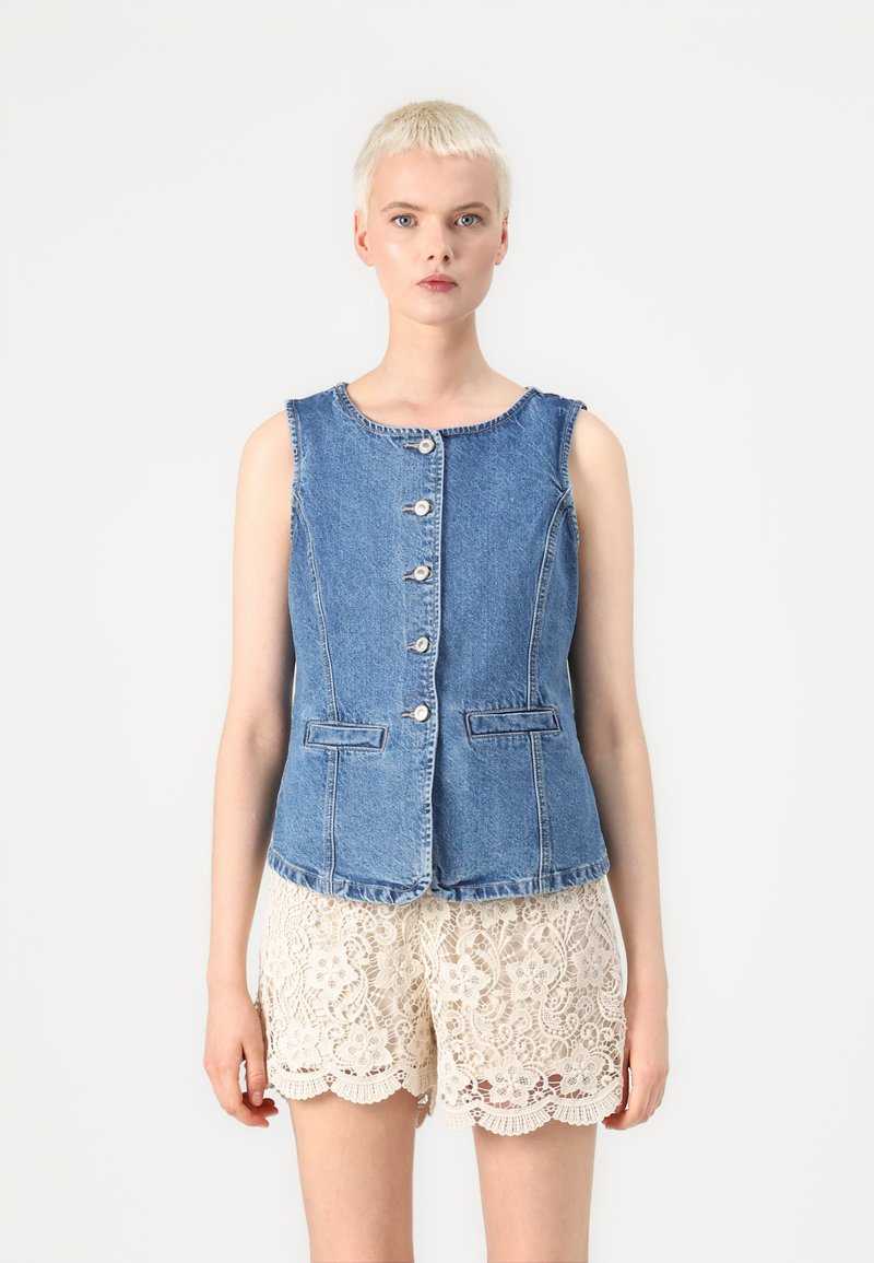 Denim vest med rund hals, frontknapper og to lommer, parret med kremfargede blonder-shorts med bølgede kanter og blomsterdesign.