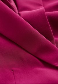 Fuchsia tyg med en jämn textur, som har mjuka draperingar och en subtil lyster. Materialet har ett enhetligt mönster och en lätt känsla.