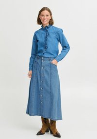 Denimskjorta med volangdetaljer vid kragen, i kombination med en lång denimkjol med knappar fram. Bruna cowboyboots fulländar looken.