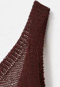 Tissu tricoté marron foncé avec un motif ouvert en maille, plié en diagonale sur un fond blanc.
