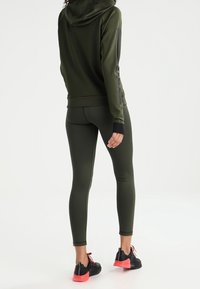 Sudadera atlética de color verde oliva con capucha, franjas negras de acento en las mangas; leggings a juego; zapatos negros con suelas rosas. Textura suave.
