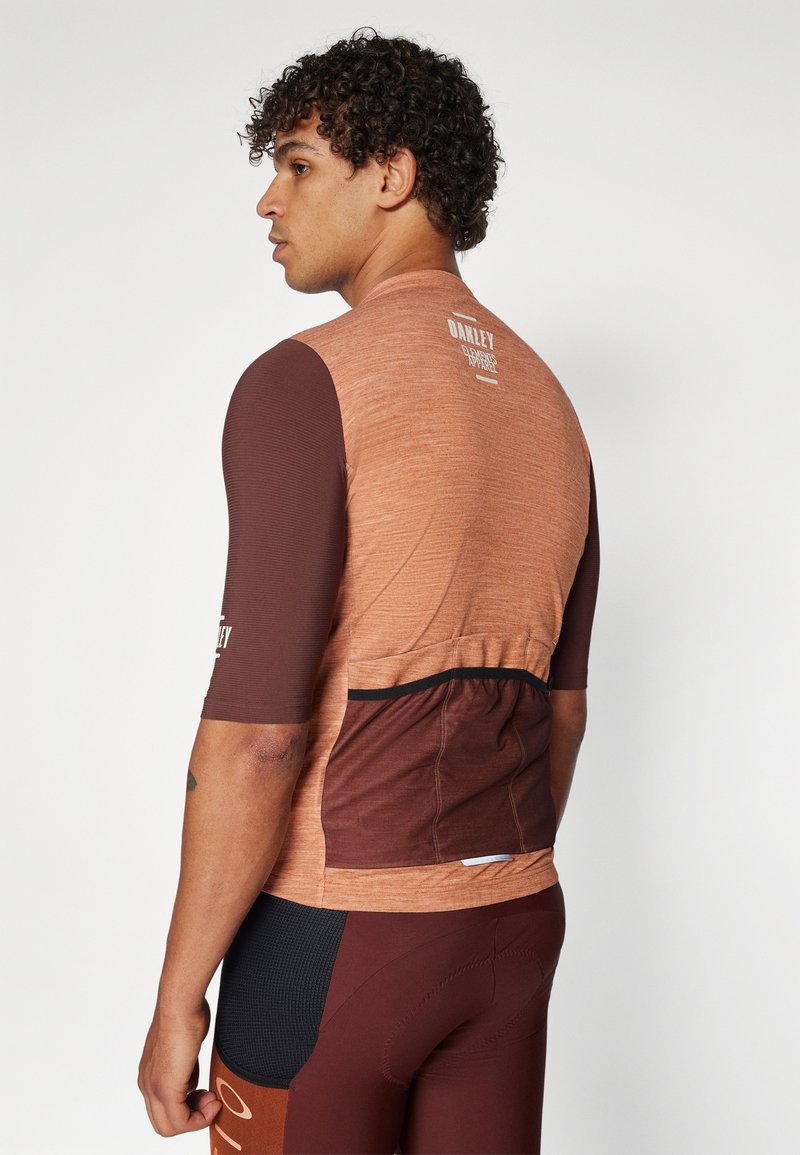 Maglia da ciclismo a maniche corte nei toni arancioni e marroni, con un tessuto testurizzato, dettagli neri e una tasca posteriore per riporre oggetti.