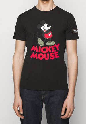 Osoba nosząca czarną koszulkę z klasycznym nadrukiem Myszki Miki i czerwonym tekstem "Mickey Mouse" z przodu, w zestawie z ciemnoniebieskimi dżinsami.