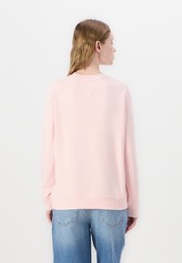 Felpa rosa chiaro con colletto e polsini a coste, texture morbida, vestibilità casual e un design posteriore pulito, abbinata a jeans azzurri.
