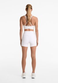 White sports bra with crisscross straps and matching high-waisted shorts. Smooth stretchy fabric with a fitted design, no visible logos.