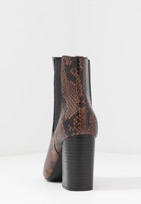 Bottine à imprimé serpent marron avec un talon épais noir et des panneaux élastiques sur les côtés ; texture lisse avec une finition brillante.