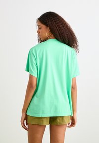 T-shirt à manches courtes de couleur vert menthe, avec une coupe décontractée, en coton. Présente un col rond et une texture lisse et unie.