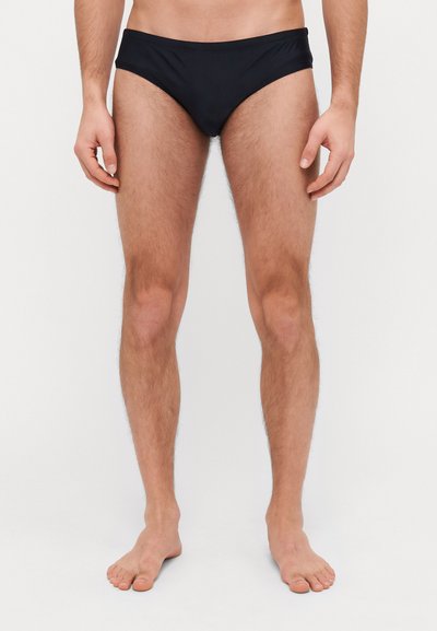 Slip da bagno neri con una texture liscia, design a vita bassa e cintura elastica. Il tessuto è leggero e aderente.