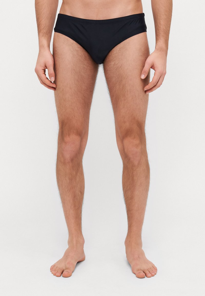 Culotte de bain noire avec une texture lisse, un design taille basse et une taille élastique. Le tissu est léger et ajusté.