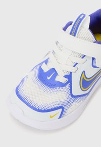 Chaussure de sport blanche et bleue avec un dessus en maille, accents jaunes et lacets blancs. Comprend un col rembourré et le logo Nike sur le côté.