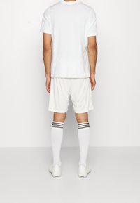 Camiseta blanca de algodón, pantalones cortos blancos, calcetas blancas hasta la rodilla con rayas negras y zapatillas deportivas blancas. Diseño minimalista, sin logotipos visibles.