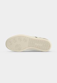 Semelle d'une basket beige clair montrant des motifs circulaires antidérapants et le mot "REPLAY" embossé près du talon.