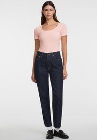T-shirt aderente rosa chiaro a maniche corte; abbinata a pantaloni jeans a vita alta blu scuro con tasche anteriori e cuciture dorate.