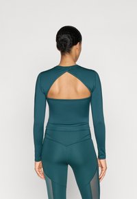 Tengerszínű, hosszú ujjú felső, kivágott hátrész designnal; sima, rugalmas anyag; párosítva hasonló textúrájú leggingssel, amely hálós panellel rendelkezik.