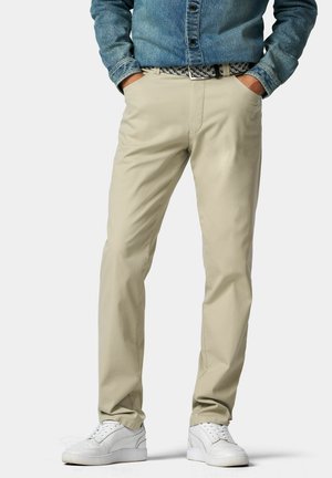 Beige katoenen broeken met een relaxte fit, voorzien van zijzakken, een rits aan de voorkant en een gebreide riem, gedragen met witte sneakers.