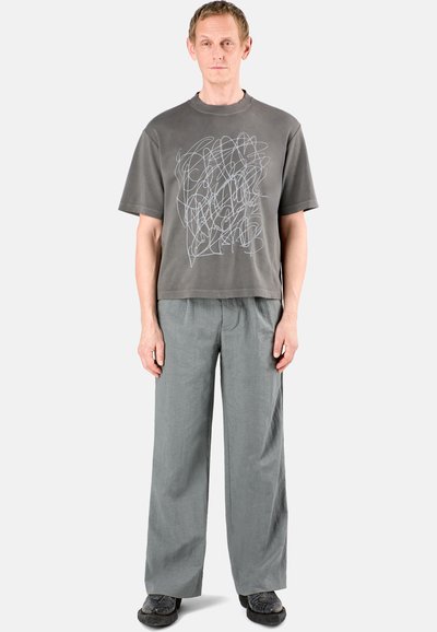 Short-sleeve gray t-shirt with abstract white graphic, paired with loose gray trousers and black shoes with textured surface.