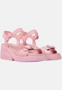 Rosa lädersandaler med urtagsdesign, justerbara ankelremmar och stort rosettdekor på tån. Har en kraftig klack för stabilitet.