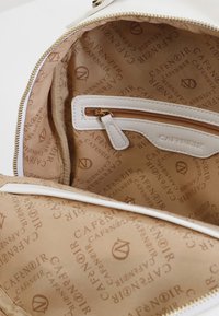 Interno di una borsa bianca con una fodera in tessuto caratterizzata da un logo ripetuto "Café Noir". Include una tasca con zip e una cerniera dorata.