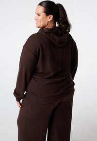 Bruine geribbelde loungewear set met een hoodie en brede broekspijpen. Zachte textuur met een relaxte pasvorm, zichtbare naden en een achterzakdetail.