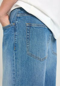 Blå denimjeans med avslappnad passform, utrustade med två bakfickor, synlig sömnad och en något sliten struktur. Enkel design.