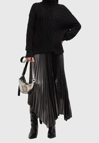 Pull noir en tricot avec texture à torsades, associé à une jupe plissée métallique noire. Les accessoires comprennent un sac à bandoulière argenté.