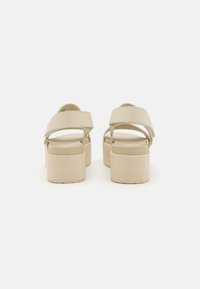 Beige platform sandals with wide straps, flat soles, and embossed "Calvin Klein" logo at the heel. Smooth texture and minimalistic design.