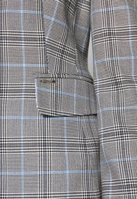 Blazer con un patrón de jaquard en blanco y negro con rayas azul claro, diseño estructurado y un bolsillo lateral con una etiqueta.