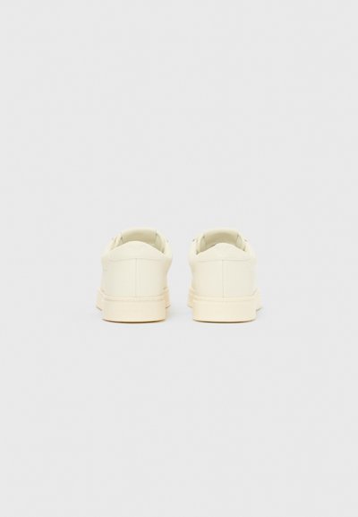 Ténis brancos com acabamento suave e mate, biqueira redonda e design de cano baixo. Apresentam uma gola almofadada e uma marcação minimalista no calcanhar.