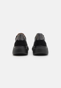 Black suede and leather sneakers with a textured rubber sole, featuring a minimal design and contrasting material accents at the heel.
