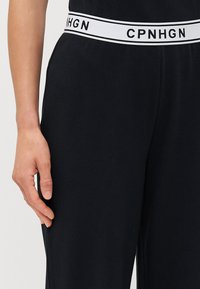 Zwarte joggings met een witte elastische tailleband waarop de tekst "CPNHGN" staat. De stof heeft een gladde textuur en een nauwsluitende pasvorm.