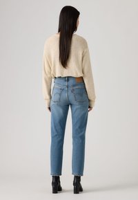 Μπεζ πουλόβερ με υφή σε συνδυασμό με ανοιχτό μπλε τζιν ψηλόμεσο, που διαθέτει δερμάτινο λογότυπο και χαρακτηριστική ραφή στην πίσω τσέπη. Μαύρα μποτάκια με τακούνι.