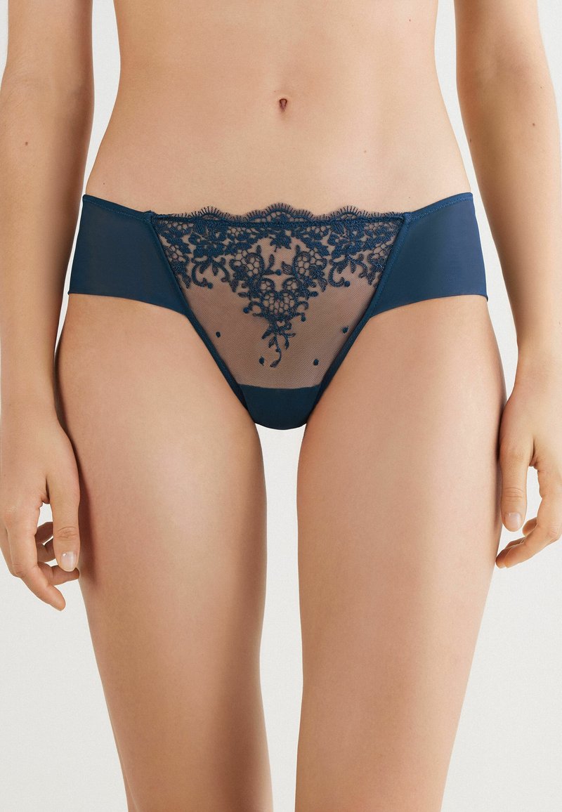 Culotte femme bleu marine avec des panneaux en mesh transparent, des détails en dentelle florale complexe et des bords en forme de vagues au niveau de la taille.