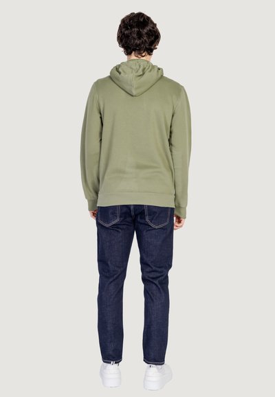 Sweat à capuche vert olive avec un design uni, tissu texturé, poignets et ourlet côtelés, associé à un jean en denim bleu foncé et des baskets blanches.