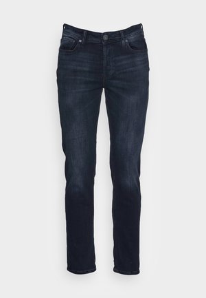 Braunes Langarmhemd mit zwei Brusttaschen, kombiniert mit blauen Jeans mit verblasstem Design und schwarzen Stiefeletten.