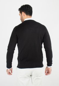 Pull noir en tissu texturé, avec des manches longues et une coupe ajustée, doté de poignets et d'une ourlet côtelés. Vue arrière uniquement.