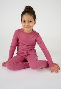Top termico a maniche lunghe rosa con texture a coste, abbinato a leggings coordinati. Dettagli di cucitura evidenti sui polsini e un piccolo logo sul petto.
