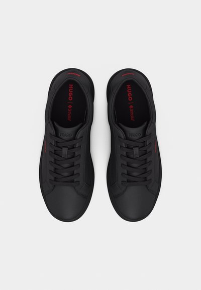 Paire de baskets basses noires avec lacets noirs, marquage rouge "HUGO" à l'intérieur et sur les côtés, vues de dessus sur fond blanc.